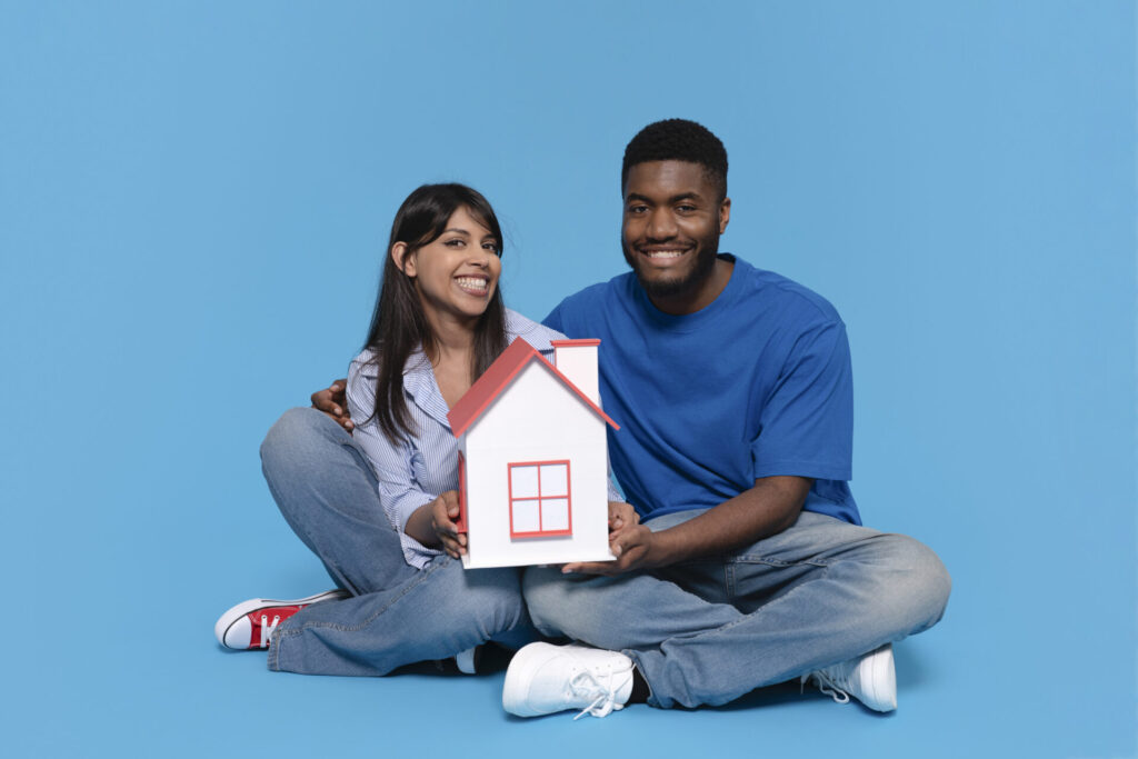 Couple souriant assis au sol, utilisé pour illustrer une fiche descriptive d’acheteur(euse) dont le rêve immobilier a été réalisé