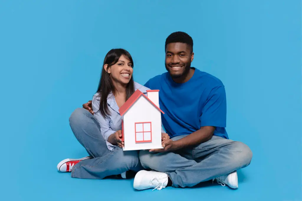 Couple souriant assis au sol, utilisé pour illustrer une fiche descriptive d’acheteur(euse) dont le rêve immobilier a été réalisé
