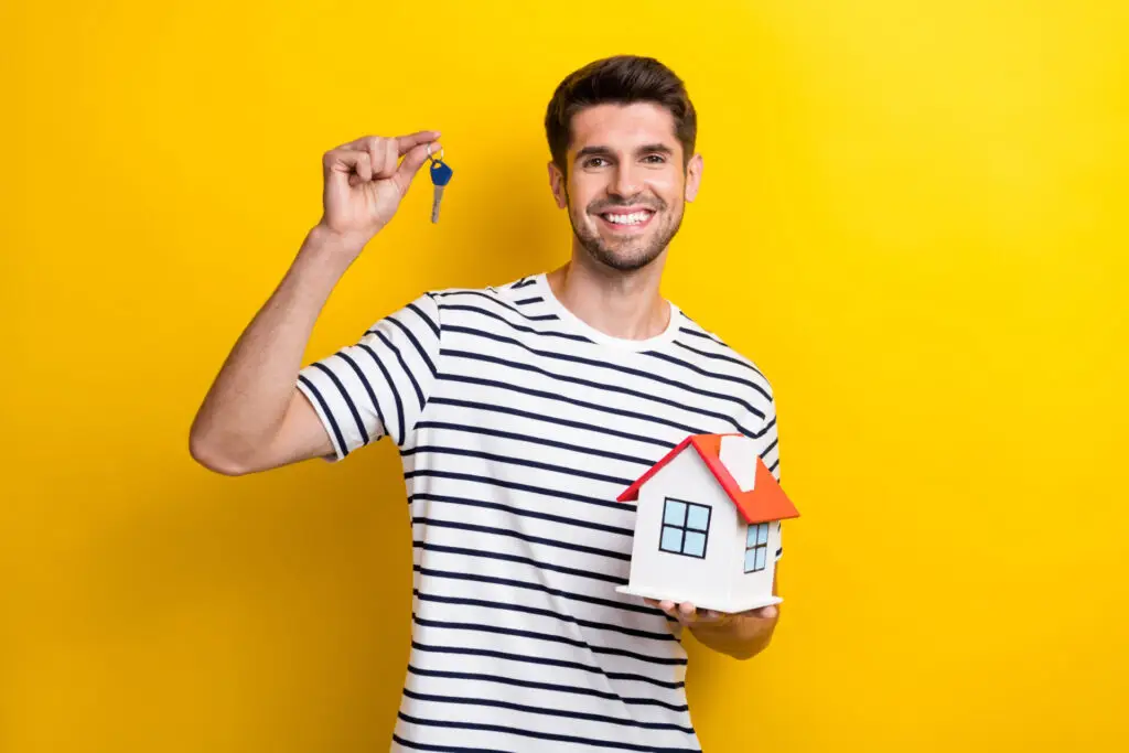 Homme tenant une clé et une maison miniature, représentant un acheteur immobilier sérieux prêt à conclure une transaction rapide.