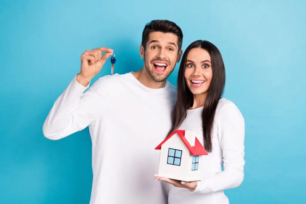 Couple tenant une maison miniature dans leurs mains, symbolisant leur recherche d’une maison dans un secteur calme offrant une vue agréable.