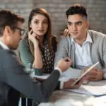 Couple en discussion avec un courtier immobilier pour préparer un achat résidentiel.