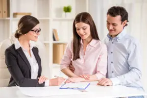Couple signant un document immobilier avec un(e) professionnel(le) lors d’une rencontre stratégique