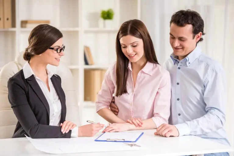 Couple signant un document immobilier avec un(e) professionnel(le) lors d’une rencontre stratégique