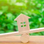 Balance en bois déséquilibrée entre deux figurines et une maison, symbolisant le déséquilibre dans une transaction immobilière.