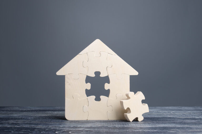 Maison en bois en forme de casse-tête avec une pièce manquante posée à côté, illustrant qu’il manque un élément essentiel à l’acheteur(euse) sans véritable représentation titre Traitement équitable en immobilier et pièce manquante de la représentation légende Une maison incomplète pour illustrer qu’un traitement équitable ne remplace pas la vraie représentation de l’acheteur(euse) description Image d’une maison en bois composée de pièces de casse-tê