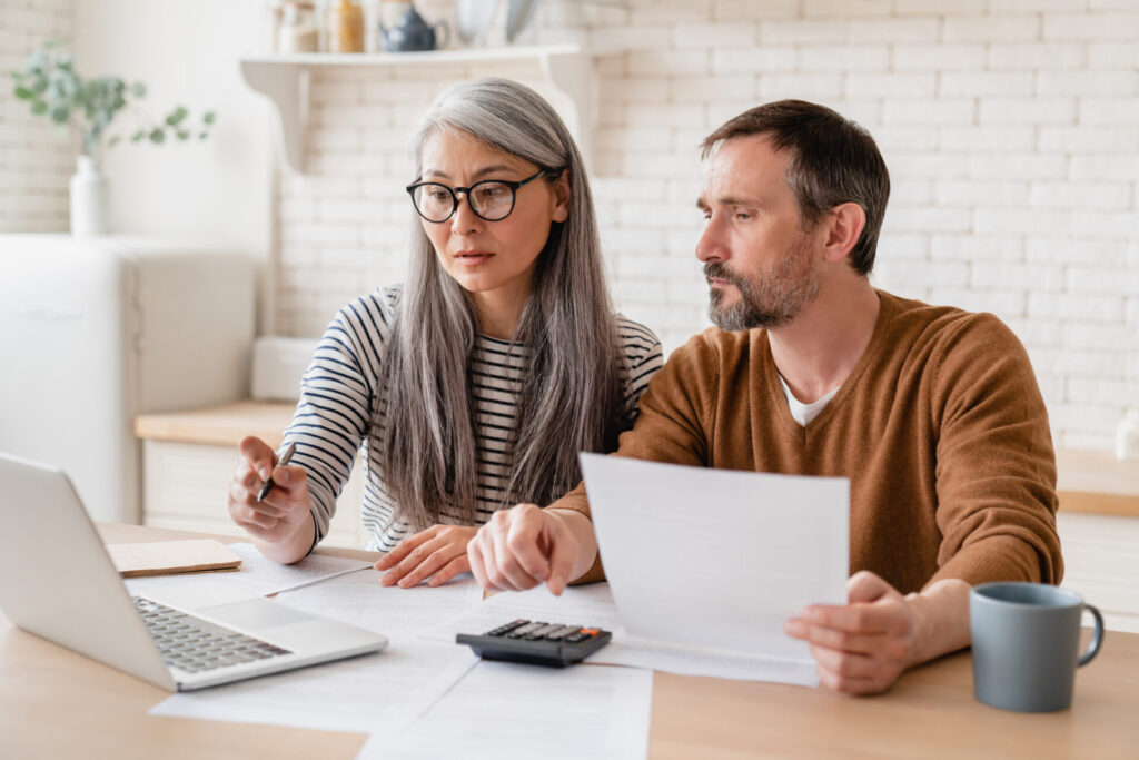 Couple à la maison en train d’examiner des documents et un ordinateur avant un achat immobilier