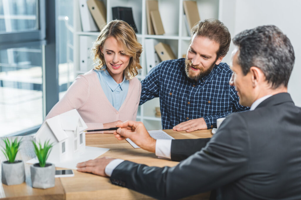 Couple en rencontre avec un courtier immobilier devant des documents et une maison miniature sur la table
