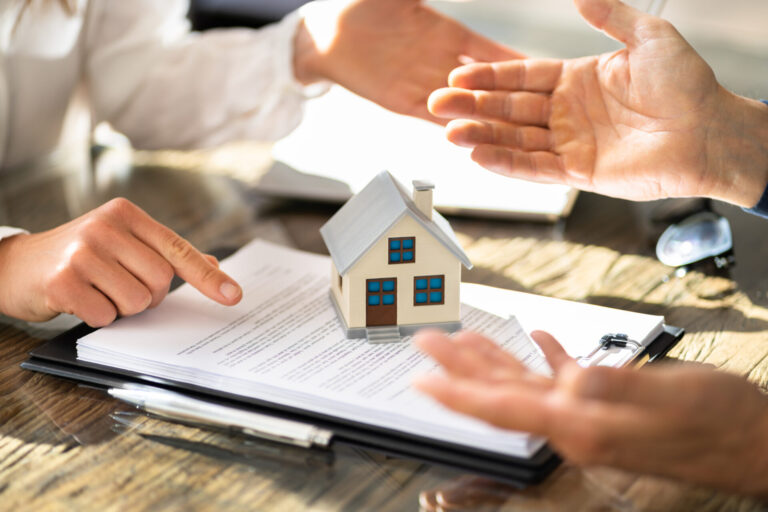 Discussion immobilière autour de documents et d’une maison miniature avant qu’un(e) acheteur(euse) ne révèle trop tôt certaines informations