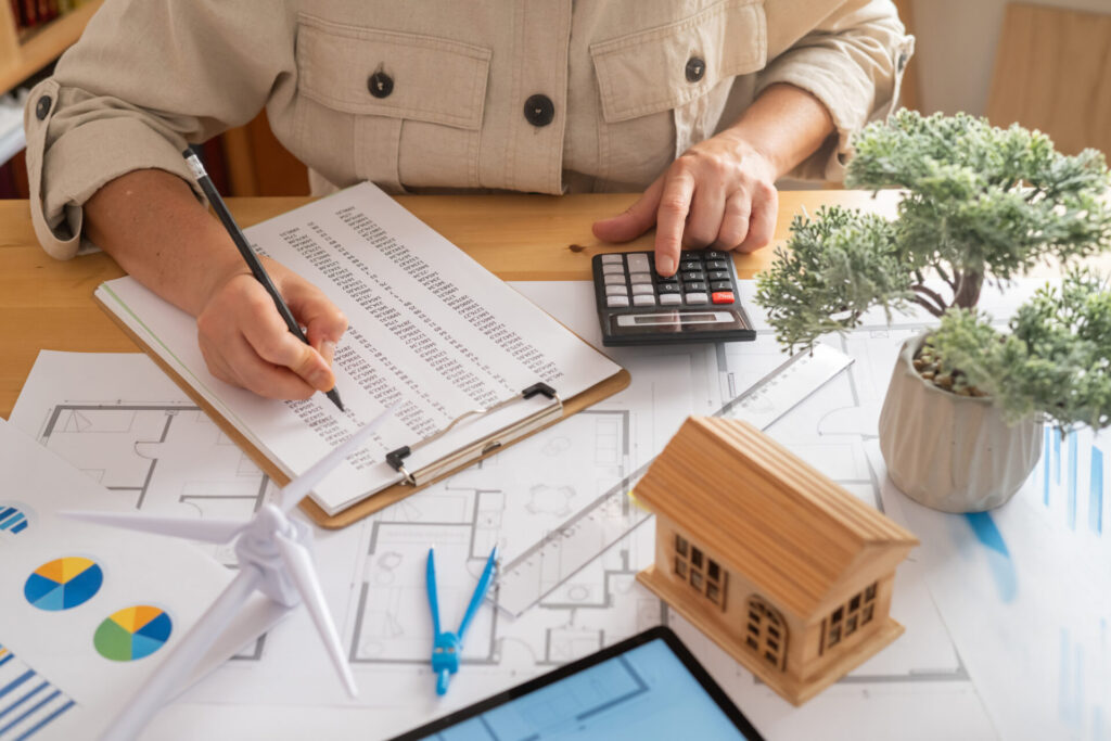 Préparation d’un projet d’achat immobilier avec calculs, documents et maison miniature avant la promesse d’achat