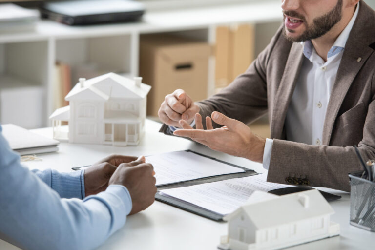 Courtier immobilier discutant du projet d’achat avec un acheteur autour de maquettes de maisons