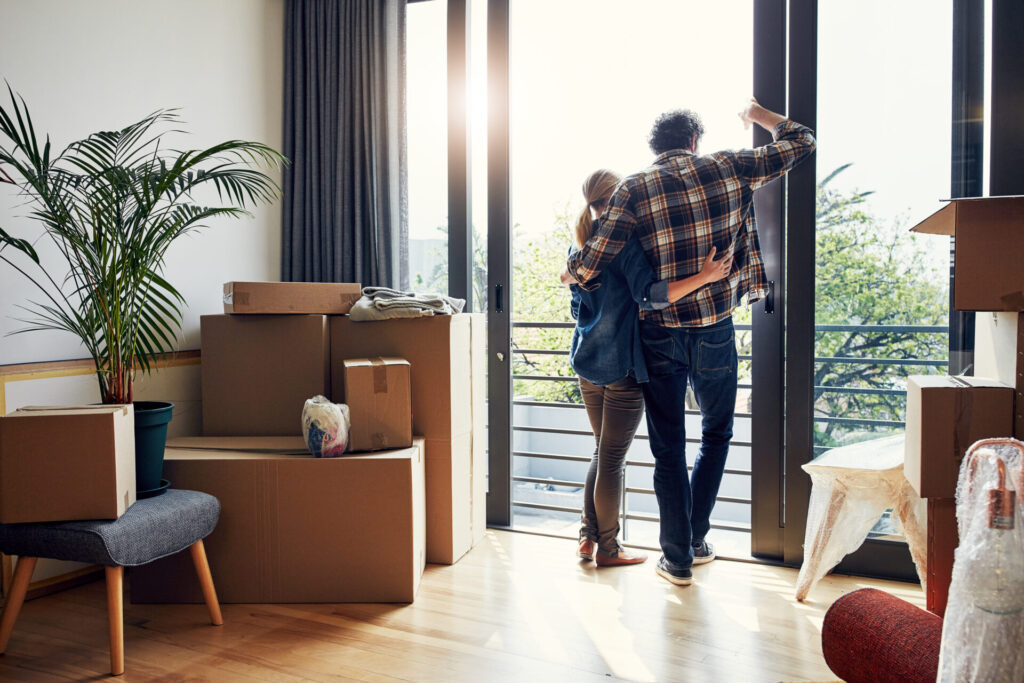 Couple entrant dans un nouveau logement avec des boîtes de déménagement, illustrant un projet d’achat accompagné du côté acheteur.